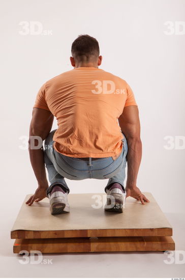 Kneeling pose orange thsirt light blue jeans of bodybuilder Harold